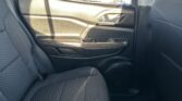 Rear passenger door interior of a dark car, showing a black textured door panel, chrome handle, and wood-style trim along the armrest with gray fabric seats nearby.