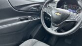 Interior front cabin of a Chevrolet, focusing on the steering wheel with logo, instrument cluster, and driver-side door controls.
