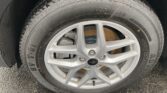 Close-up of a car tire mounted on a silver alloy wheel, with visible tread and a rusted brake rotor behind it.