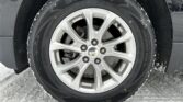 Close-up of a Chevrolet alloy wheel and tire with snow along the tread and ground beneath.