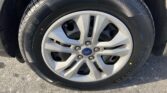 Close-up of a car tire mounted on a silver alloy wheel with a Ford center cap showing five-spoke design and lug nuts