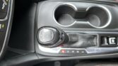 Center console in a car showing a gear shift lever and two cup holders nearby.