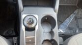 Center console of a car showing a rotary gear selector (P, R, N, D, L) and cup holders; surrounding trim in brushed metal finish with a small electronic parking brake button nearby.