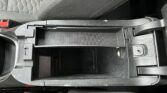 Open center console storage tray in a car, currently empty with surrounding upholstery and red seat belt buckle nearby