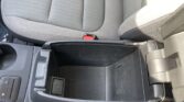 Center console in a car with a cup holder, small storage bin, and a red seat belt buckle near the front of the seat rail.