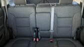 Interior of a car showing the back seats in dark gray fabric with a patterned texture; three-seat bench in view, with visible seat belts and headrests, red buckle tongues at the bottom.