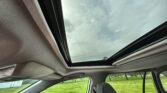 Open panoramic sunroof in a car, showing blue sky with clouds and a green lawn outside.