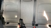 Rear car seat row with three seating positions in gray fabric; visible three-point seat belts, red buckle in the middle, and headrests at the top.