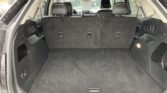 Rear cargo area of an SUV with folded second-row seats upright and a wide open trunk hatch showing carpeting and small storage compartments on sides