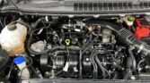 Front half of a vehicle's engine bay with a tangle of hoses, wires, and components; coolant reservoir visible on the left and the battery on the right.