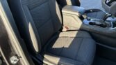 Inside a car showing black fabric front seats with white stitching, center console, armrest, gear shifter, and cupholders.