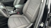 Front interior of a car showing two cloth seats with textured patterns and stitching, center console, and steering wheel visible on the left side.