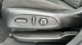 Seat adjustment panel on the side of the driver’s seat with a horizontal lever, a small vertical lever, and a round knob for lumbar support, in black interior fabric with yellow stitching.
