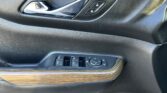 Close-up of a car interior door panel with a chrome door handle and lock/unlock buttons beside it on black textured surface, wood trim below.