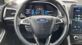 Close‑up of steering wheel in a Ford, with digital instrument cluster and large touchscreen visible.
