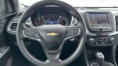 Front interior shot of a Chevrolet car showing the steering wheel, instrument cluster, and center touchscreen display. Gear shifter and climate controls visible to the right.