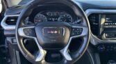 Close-up of a GMC steering wheel and instrument cluster seen from the driver’s seat, with an infotainment screen to the right and climate controls below.