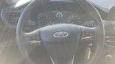 Driver's view of a Ford steering wheel with built-in controls, instrument cluster, and center display, sunlight glare across the dashboard.
