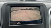 Rearview camera display showing a parking lot behind the vehicle with yellow guiding lines and a red line indicating distance to objects.