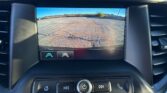 Car rearview camera display showing orange guiding lines over a cracked asphalt parking lot.