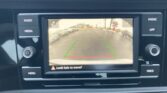 Rearview camera display showing a street behind the car with parked cars on both sides; green guide lines and a red line indicate distance.
