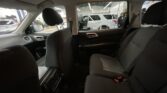 Interior of a car looking toward a workshop; a white SUV is being serviced outside with a mechanic nearby, through the open door window.