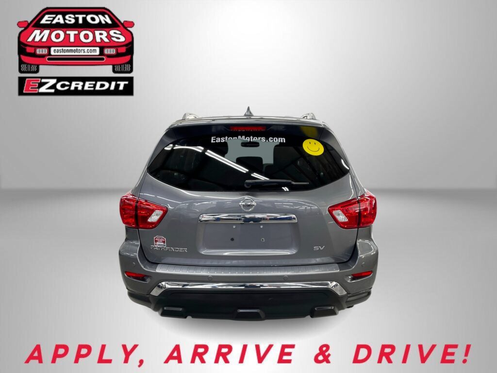 Rear view of a gray Nissan Pathfinder with EZCredit logo on left and a yellow smiley sticker on rear window, showroom backdrop.