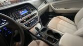 Interior of a car showing the front passenger area with a beige seat, center console, and dashboard controls lit up, including a touchscreen infotainment system and climate controls.