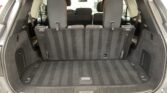Cargo area of an SUV with the third-row seats upright, showing a spacious, charcoal carpeted trunk and rear seats visible through the hatch.