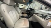 Front interior of a white car with light-beige seats, steering wheel, and center console, taken from the rear passenger area.