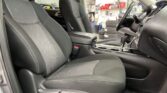 Front car interior with black fabric seats and center console, gear shifter visible, in a workshop with tires in the background.