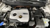 Engine bay of a hybrid car with a silver cover labeled 'hybrid' in the center; orange high‑voltage cable visible beneath the hood.