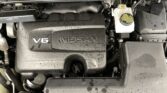 Nissan V6 engine bay with a damp engine cover labeled V6 NISSAN and a visible white coolant reservoir on the right.
