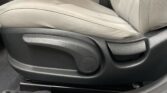 Close-up of a car seat adjustment knob and lever on a beige fabric seat.