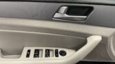 Interior of a car door with the silver door handle and window/mirror control panel nearby on a textured gray door panel