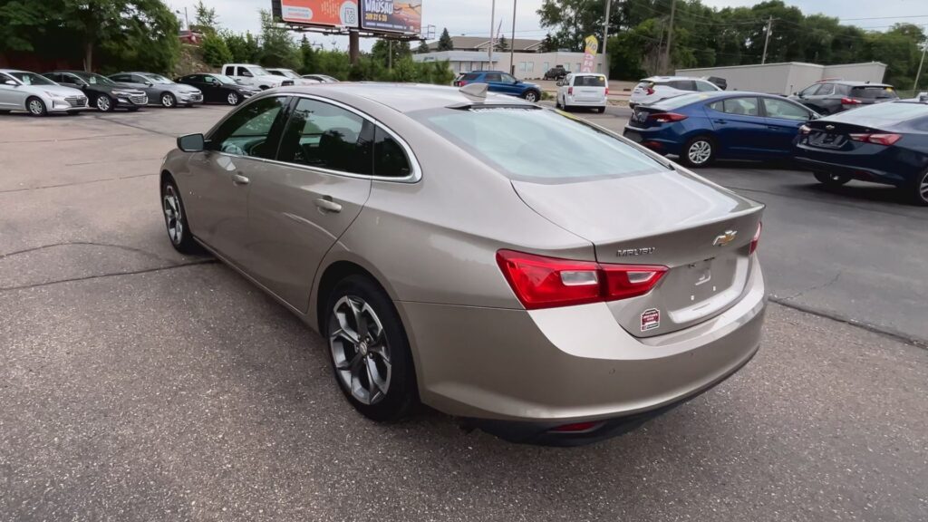 Black Dodge sedan inside a showroom, yellow round sticker on the windshield, another silver car visible in the background.
