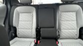 Rear car seats with light gray quilted upholstery and black center console/armrest in the upright position, view from the back seat.