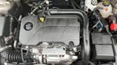 Engine bay with a black Ecotec cover, yellow oil dipstick, and white coolant reservoir on the right; red battery terminal visible nearby.