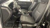 Front seats and steering wheel of a black car, shown from the open driver's side door at a showroom dealership.