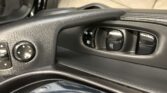 Close-up of a car driver's door panel showing window controls, mirror adjustment knob, and textured armrest.