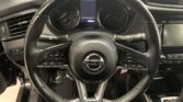 Steering wheel with Nissan emblem, center digital display between analog gauges, and control buttons on both sides; dashboard vents visible to the left and right.