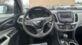 Driver's-seat view of a Chevrolet interior: steering wheel, center touchscreen, and gear shifter with a parking lot of SUVs outside.