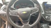 Close-up of a Chevrolet steering wheel with integrated controls, instrument cluster, and an inset touchscreen infotainment display to the right-front of the dashboard.