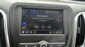 Car infotainment screen showing radio 100.3 Home BY OLD DOMINION in a parked-car interior with outside row of SUVs and cars visible through windshield