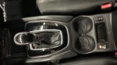 Center console of a car showing the gear lever, two cup holders, and a red seatbelt buckle nearby.