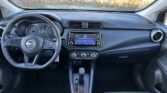 Interior view from the driver's seat in a Nissan, showing steering wheel, instrument cluster, and center touchscreen infotainment unit with climate controls below.