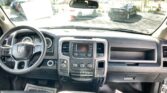 Front interior of a pickup truck from the back seat, showing the steering wheel, center console, and dashboard. A rearview mirror is overhead and the windshield looks out onto a parking lot with other cars.