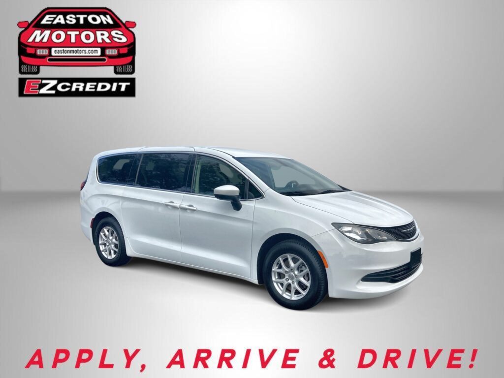 White minivan in a studio-like setting with an EZ Motors/EZ Credit logo on the wall to the left and bold red text reading 'APPLY, ARRIVE & DRIVE!' at the bottom.
