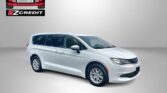 White minivan in a studio-like setting with an EZ Motors/EZ Credit logo on the wall to the left and bold red text reading 'APPLY, ARRIVE & DRIVE!' at the bottom.