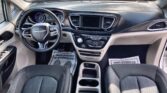 Front interior of a modern SUV: steering wheel with Chrysler emblem, illuminated dashboard gauges, blank center touchscreen, and cupholders between the seats.